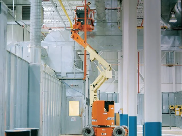 Plataforma elevadora en una fábrica con paredes de metal y tuberías en el techo.