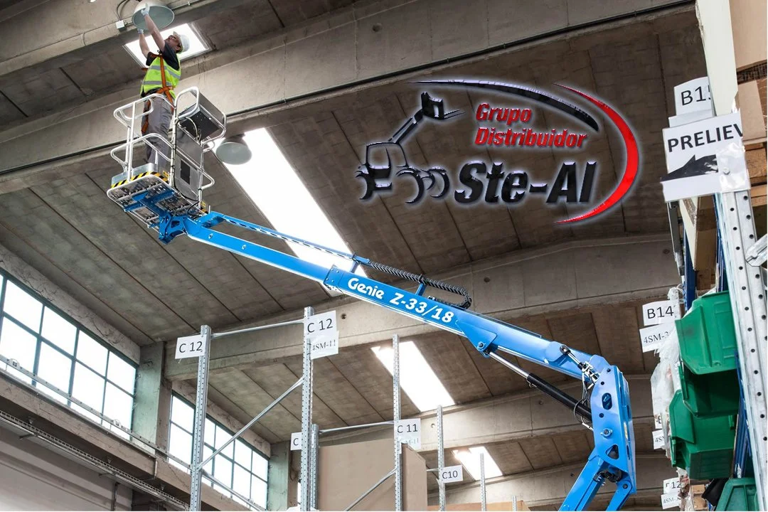 Trabajador en una plataforma elevadora instalando un cartel en un almacén con techo de concreto y grandes ventanas, el cartel dice 'Grupo Distribuidor Ste-AI'.